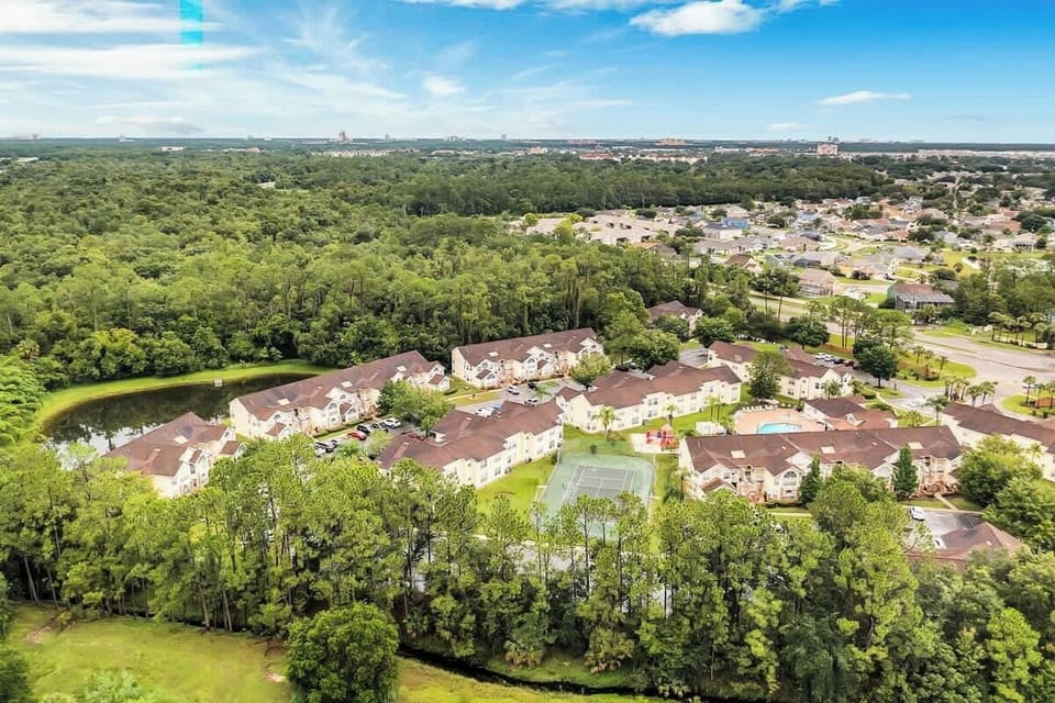 Aerial view of a residential community surrounded by lush greenery and featuring a tennis court and pool area.