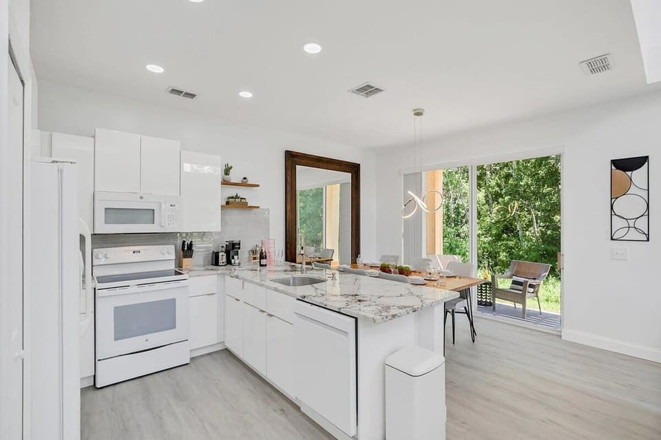 Modern kitchen with marble countertops and a dining area overlooking a green backyard.