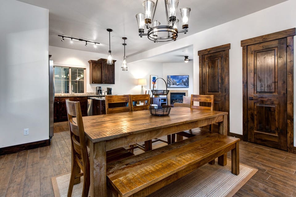 Gather around the rustic wooden dining table that comfortably seats 6 guests. With a bench on one side and chairs on the other, it's perfect for family meals or game nights. Set beneath elegant lighting and close to the kitchen for easy serving.