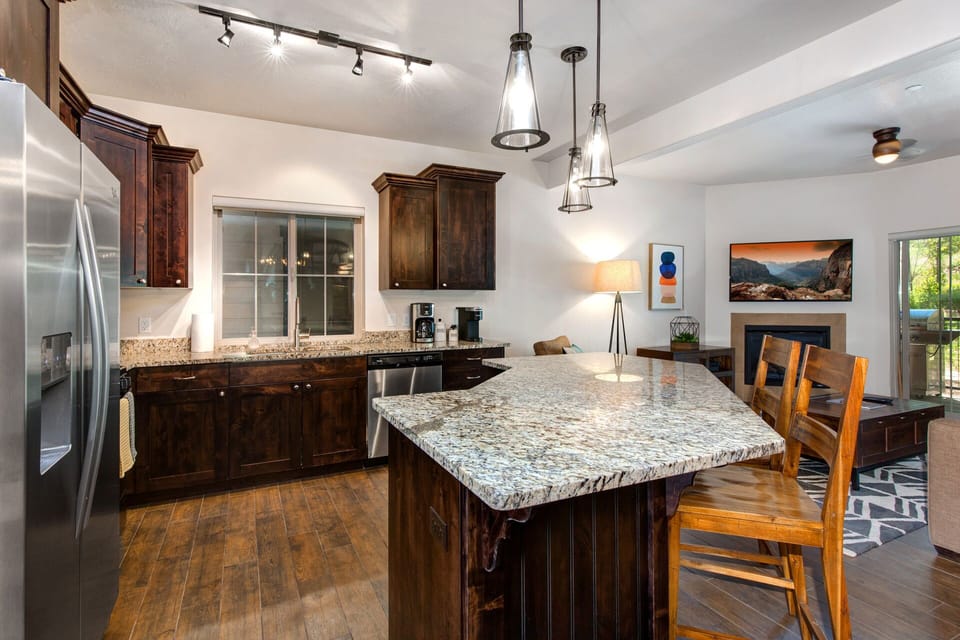 A stylish kitchen with granite countertops and rich wood cabinetry. The island seats 4 and offers the perfect space for breakfast, casual dining, or entertaining while cooking. Modern lighting and stainless appliances complete the look.