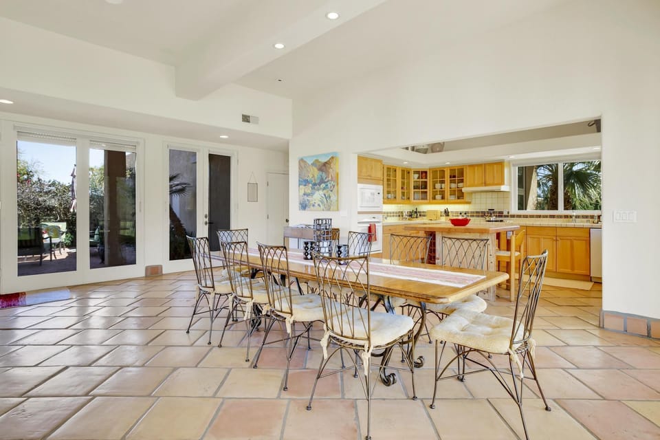 A bright and inviting open-concept dining and kitchen area with a blend of rustic and modern elements. The floor is covered with large terracotta tiles, adding a touch of rustic charm.