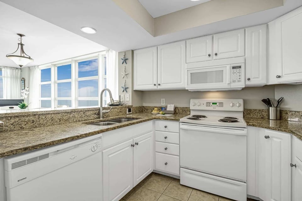 Bright kitchen with granite countertops, white cabinetry, full-size appliances, and ocean views flowing in from the nearby living area.