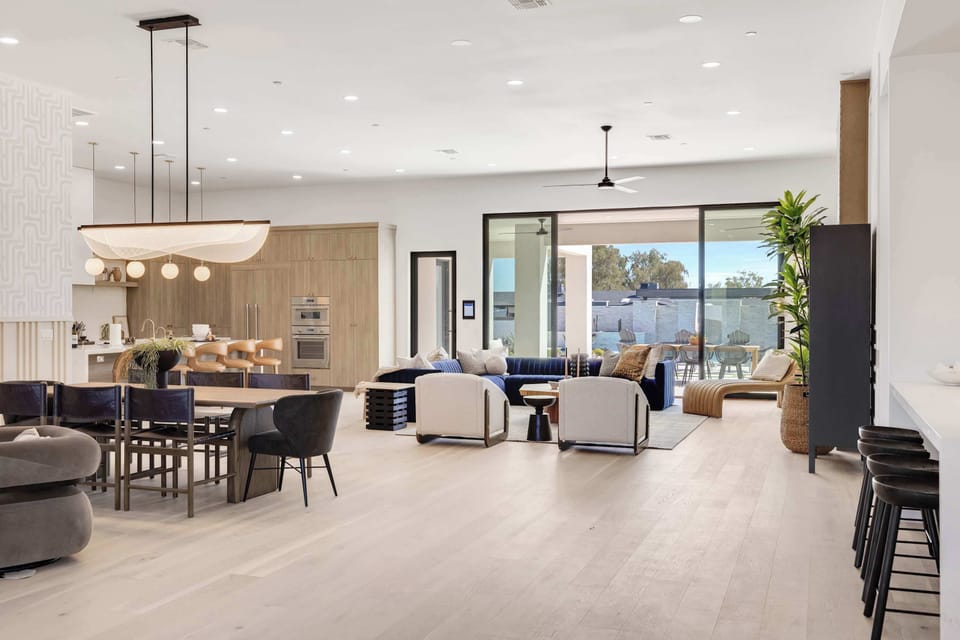 Expansive great room with elegant dining area, designer lighting, and direct backyard access through floor-to-ceiling sliding glass doors.