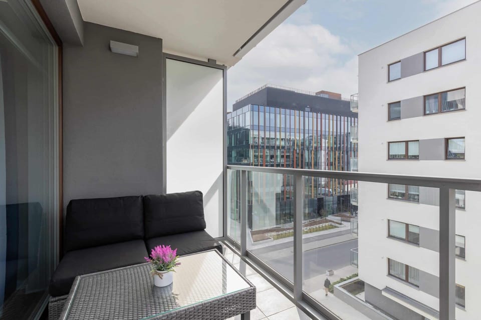 A balcony with seating, offering a view of a contemporary urban setting.
