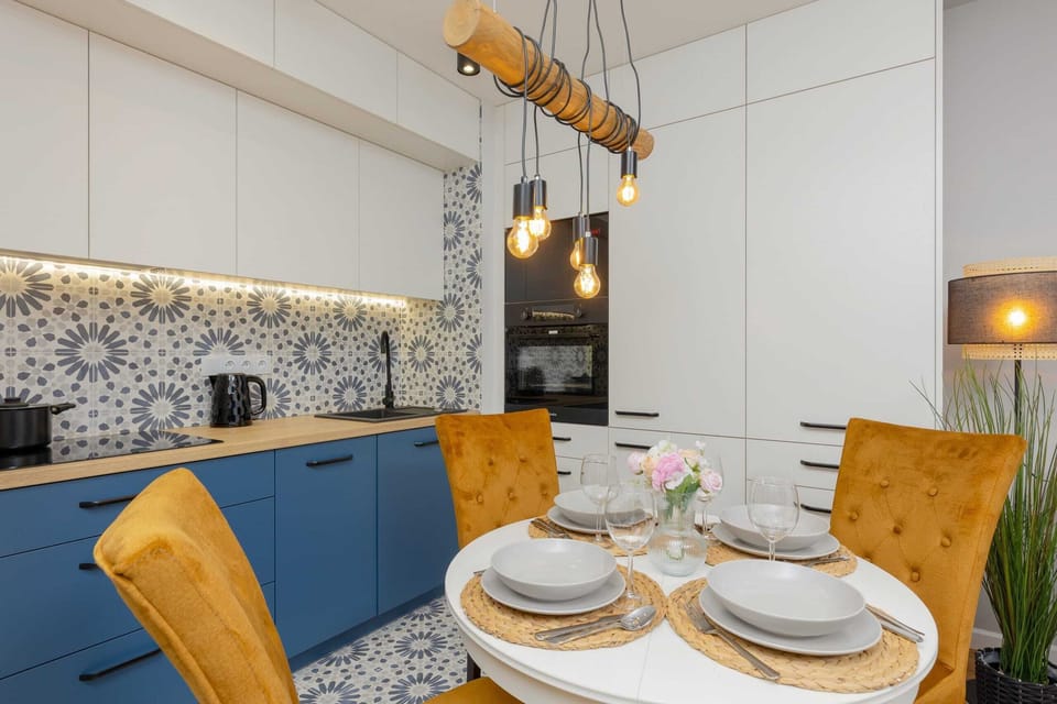 A bright dining area with a round table, blue and yellow accents, and elegant place settings.
