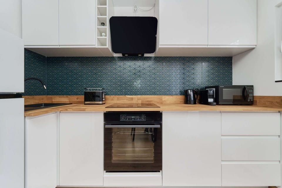 A modern kitchen featuring a turquoise tiled backsplash, white cabinets, and stainless steel appliances.
