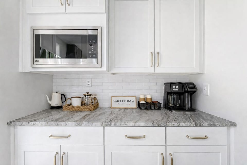 Convenient coffee bar with built-in microwave, drip coffee maker (ground coffee and pods included), kettle, french press, and stocked supplies (sugar, half & half, honey, paper cups and lids)—perfect for slow mornings and quick refills.