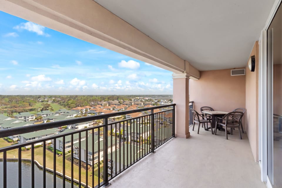 Spacious covered balcony with outdoor dining table overlooking expansive neighborhood views under blue skies.