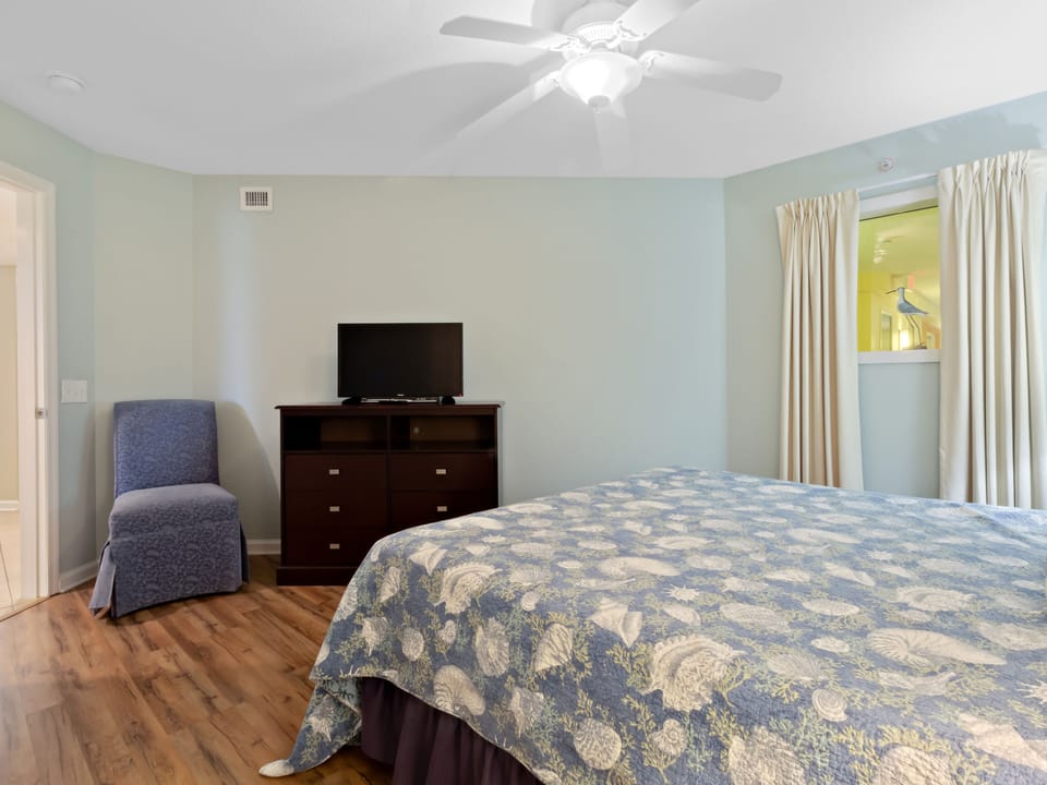 Your peaceful bedroom features a comfy blue chair for evening reading and entertainment center for unwinding after coastal adventures.