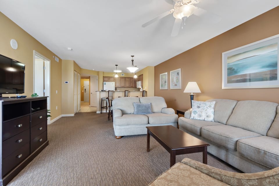 Unwind in your spacious living room with plush seating, entertainment center, and open kitchen beyond.