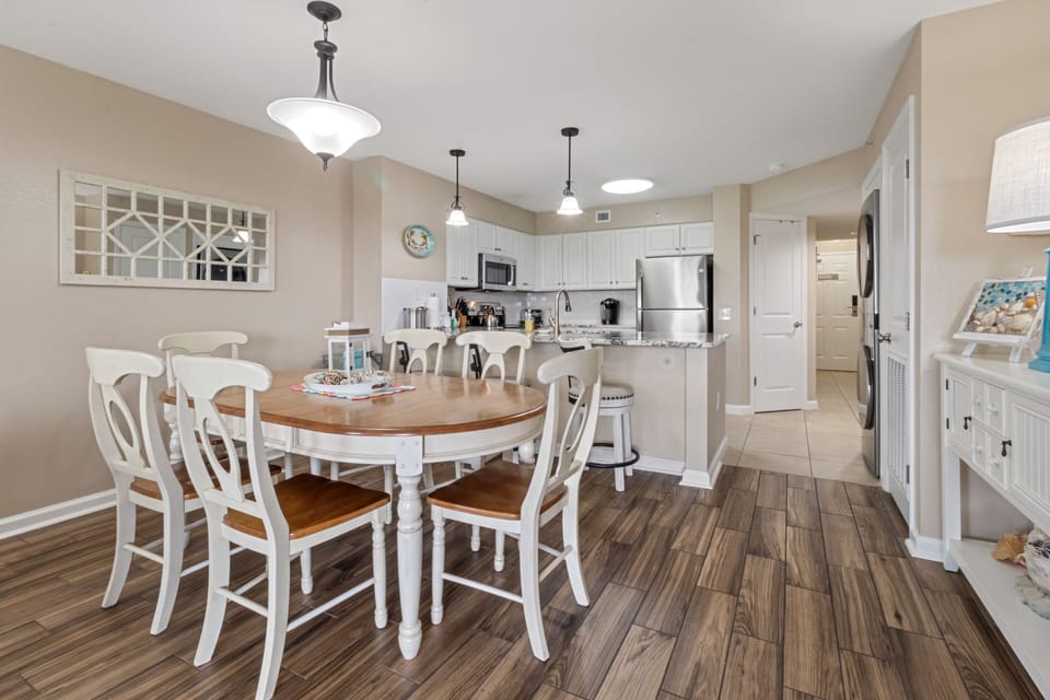 Step into your bright coastal dining space where warm wood floors meet elegant white furnishings, perfect for gathering around the farmhouse table.