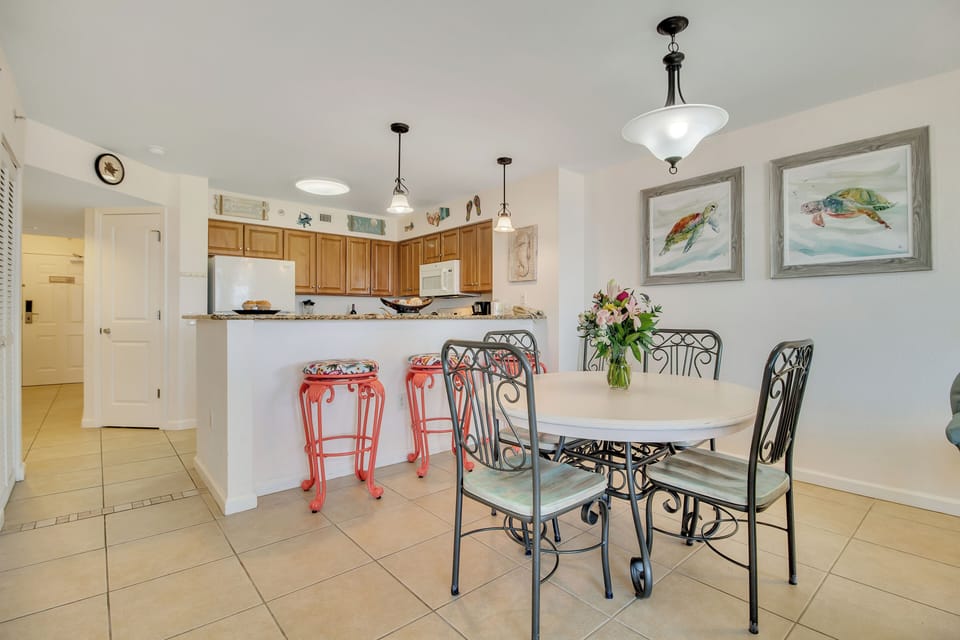 Your open kitchen flows into a bright dining area where colorful stools and coastal art create a cheerful gathering space for shared meals.