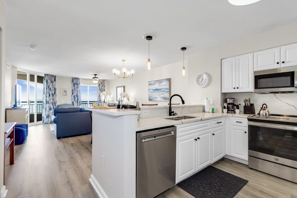 Your open-concept kitchen flows seamlessly into the living space, featuring white cabinetry and ocean views through floor-to-ceiling windows.