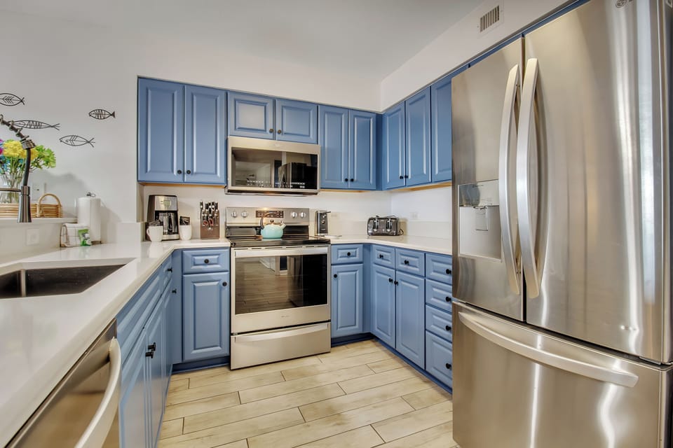 Whip up your favorite meals in this charming coastal-themed kitchen featuring cheerful blue cabinets and modern stainless steel appliances.