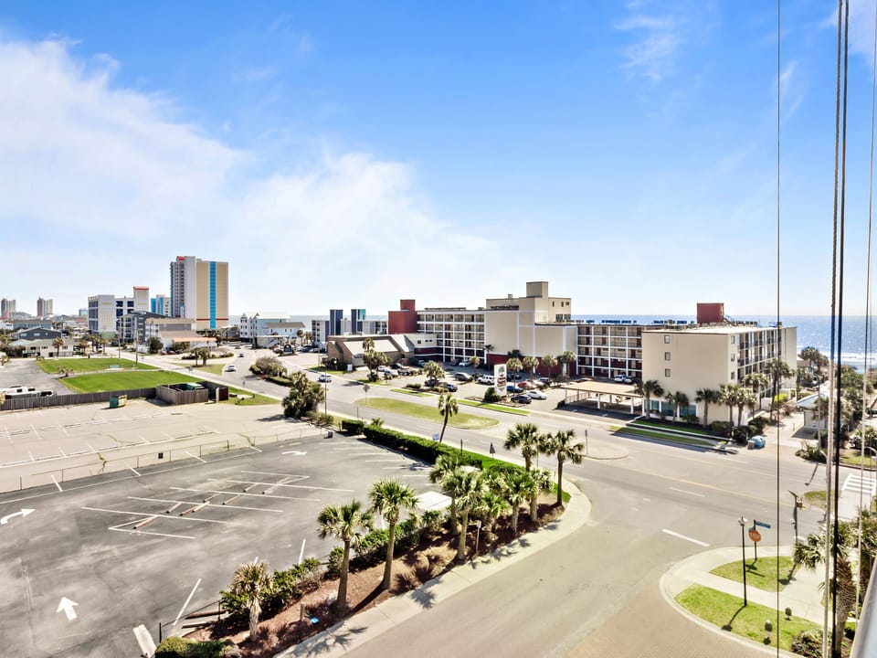 Elevated view of the coastal area featuring hotels, palm trees, and beachfront development under blue skies.