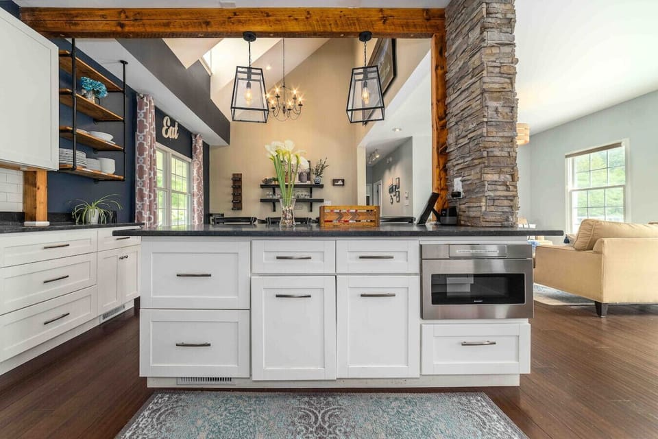 Enormous soap stone island with built in microwave, antique wood beam and custom stone wall.  Custom Industrial Wall Mount Iron Pipe shelves stocked with plenty of dishes