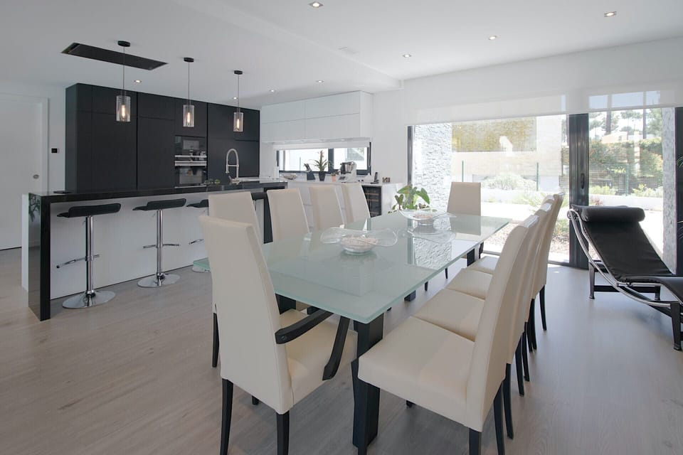 Open-plan dining and kitchen area with glass table and cream upholstered chairs — Villa Alfazema IV, luxury holiday villa in Herdade de Aroeira