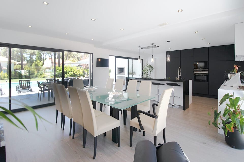 Modern open-plan dining and kitchen with glass dining table — Villa Alfazema IV, luxury holiday villa in Herdade de Aroeira