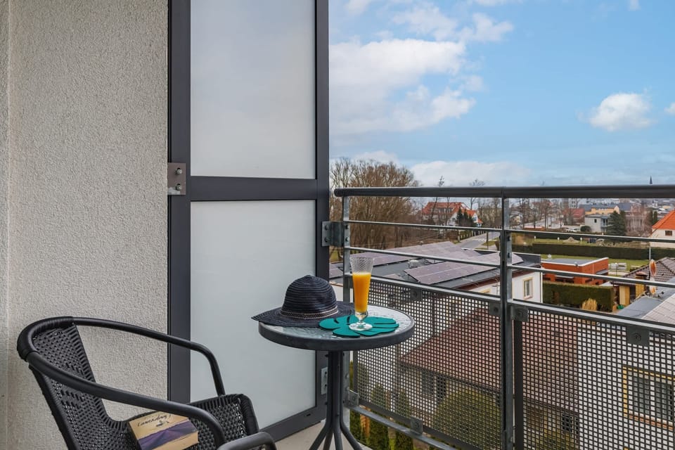 A small balcony with a black table and chair, overlooking a landscaped outdoor area.