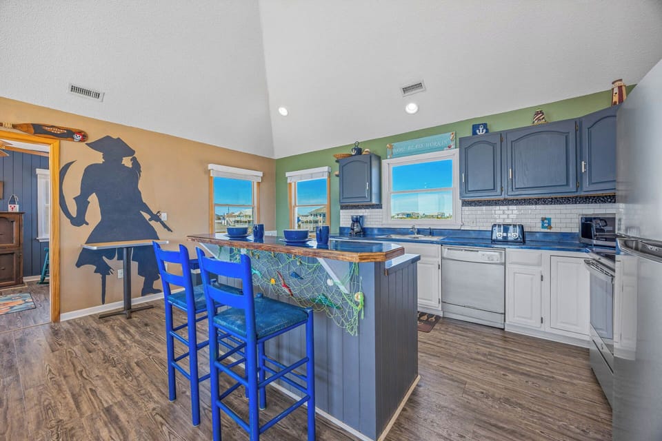 Your coastal-themed kitchen invites you to gather at the island, where bright blue stools and a playful mermaid mural set a cheerful, beachy tone for cooking and sharing meals together.