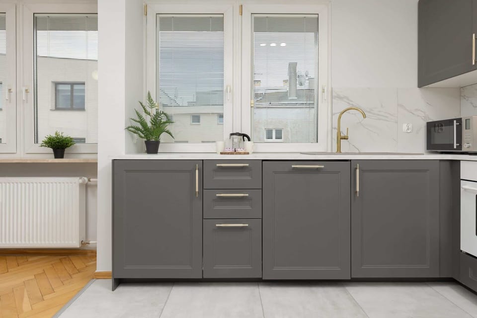 A sleek kitchen featuring a combination of gray cabinets, a stovetop, and white tiled walls.