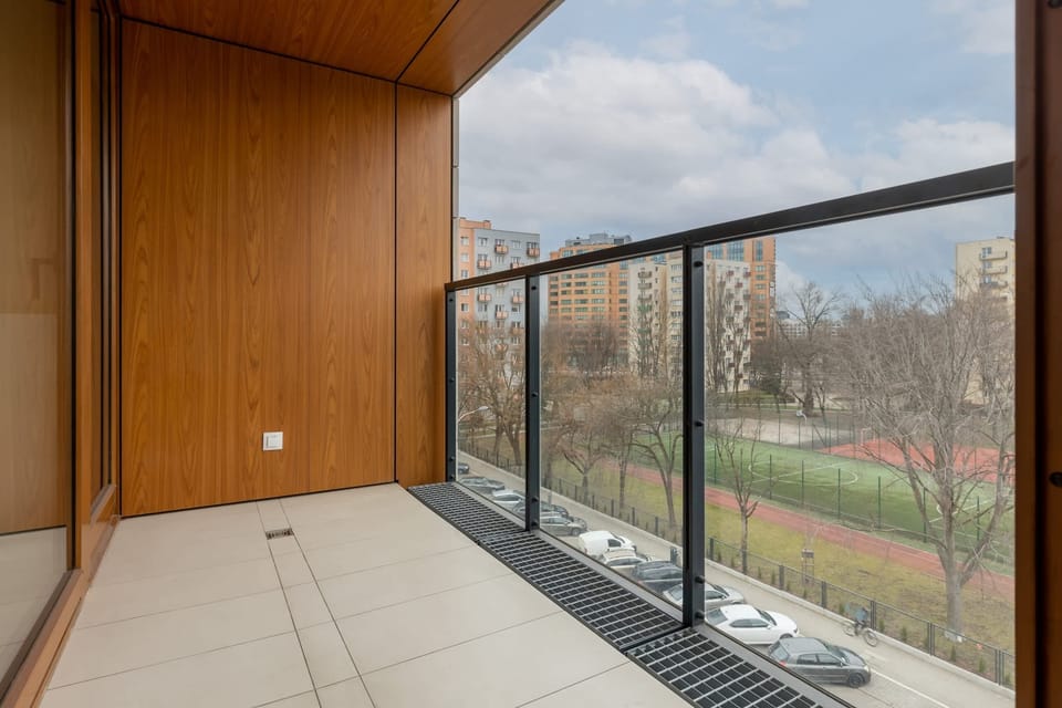 A balcony featuring wooden paneling on the ceiling and floor, offering a cozy outdoor area. The view includes greenery and an urban landscape.