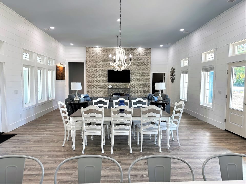 View of Dining Table tp Living Room with brick wall, TV, windows view pool area.