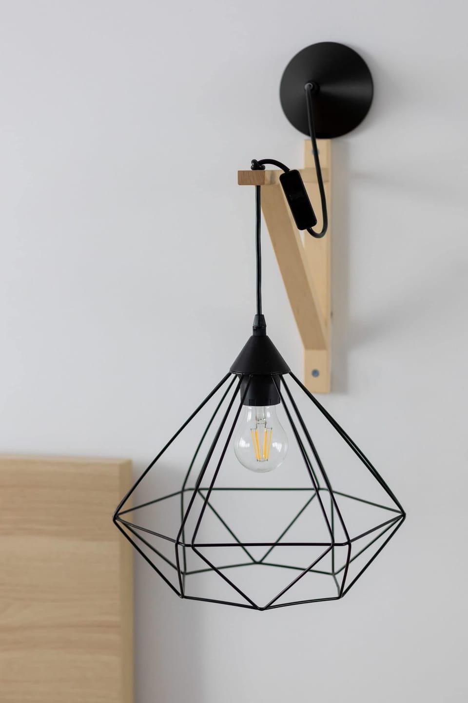 A minimalist wall hook with a geometric design, hanging near a wooden shelf.