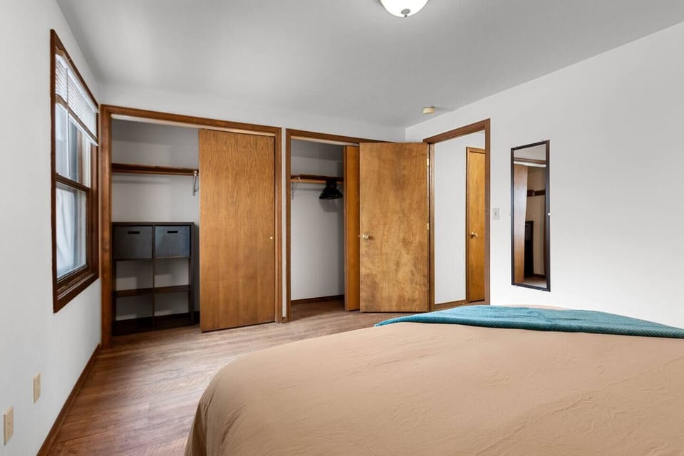 The spacious bedroom features a comfortable, king bed with extra pillows, nightstands with lamps, an alarm, full-length mirror, and ample closet space.