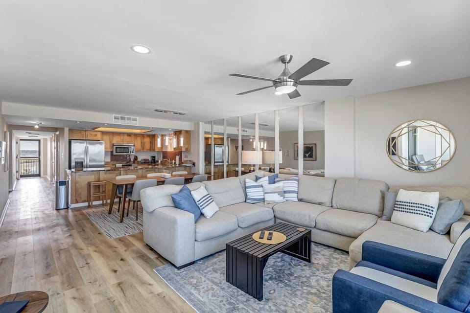 - Relax in a spacious living room with plush sectional seating, coastal decor, & direct sightlines to the kitchen & dining space
- Modern mirrors reflect light, enhancing the open feel
- Warm, welcoming place to gather after beach adventures