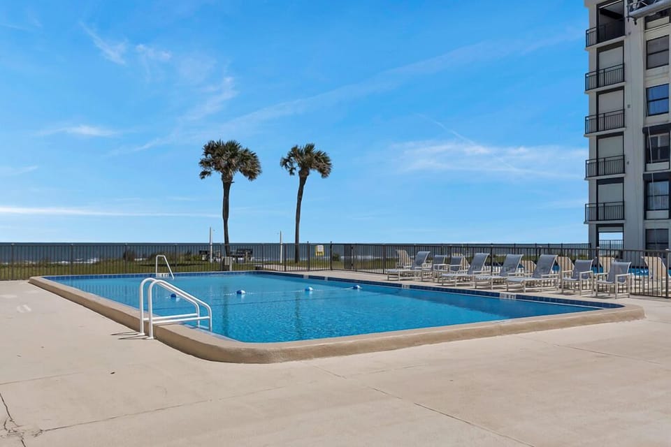 Spacious pool deck with palm trees and endless ocean in the background.