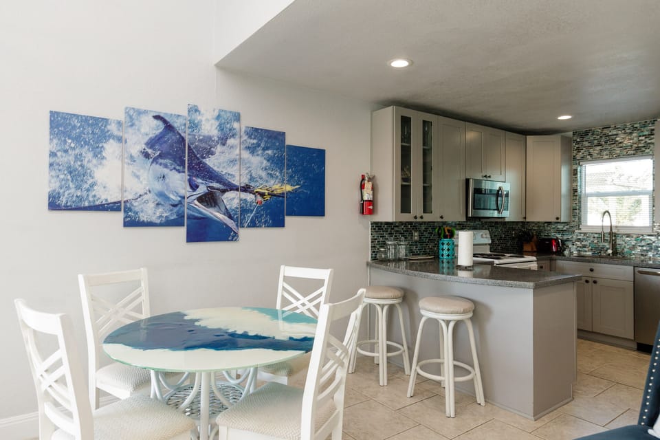 Your open-concept kitchen and dining space features modern appliances and coastal artwork, perfect for preparing meals together.