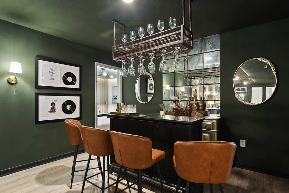 Elegant mirrored bar with leather stools, record art, hanging glasses, and cozy vibe
