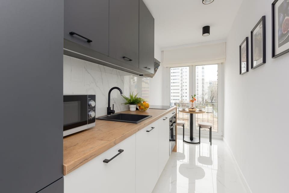 A sleek kitchen with wooden countertops, grey cabinets, and a small dining nook by the window.
