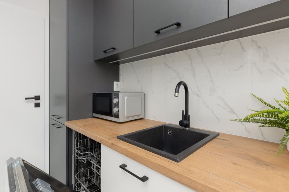 A modern kitchen with wooden countertops, sleek black sink, and grey cabinetry, offering a stylish and functional cooking space.
