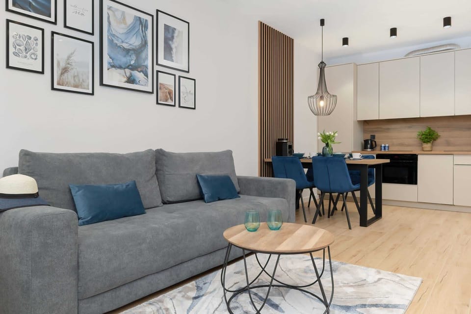 A combined living and dining area with a grey sofa, artistic wall decor, and a well-equipped kitchen.

