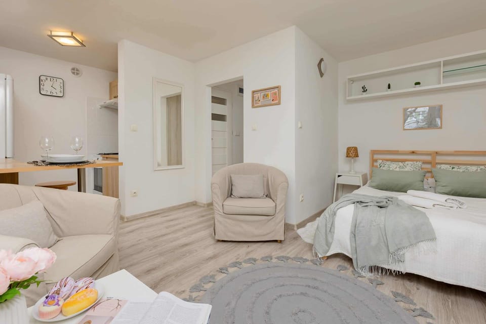 A cozy, multifunctional space combining a living room and a sleeping area. It features a comfortable beige armchair, a green blanket, and soft lighting for a relaxing atmosphere.
