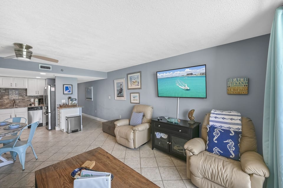 Relax in your coastal-themed living space with comfortable leather seating, large flat-screen TV, and open layout connecting to the modern kitchen.