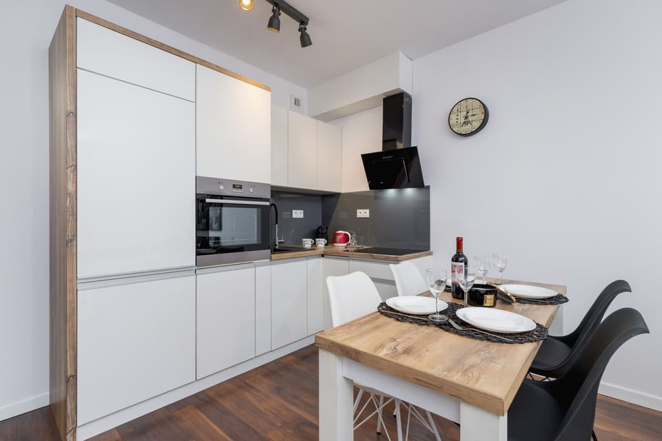 A sleek kitchen with modern appliances, including a built-in oven, microwave, and ample storage in white and black cabinetry. The kitchen opens up into the living and dining area.