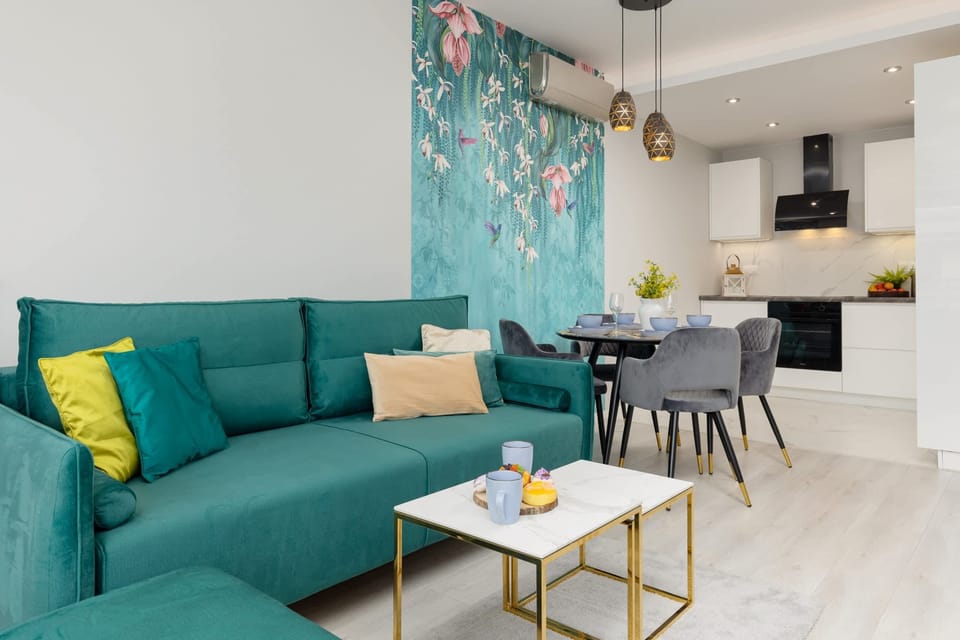 A living room with a teal sofa, golden decor, and an open connection to the dining area.
