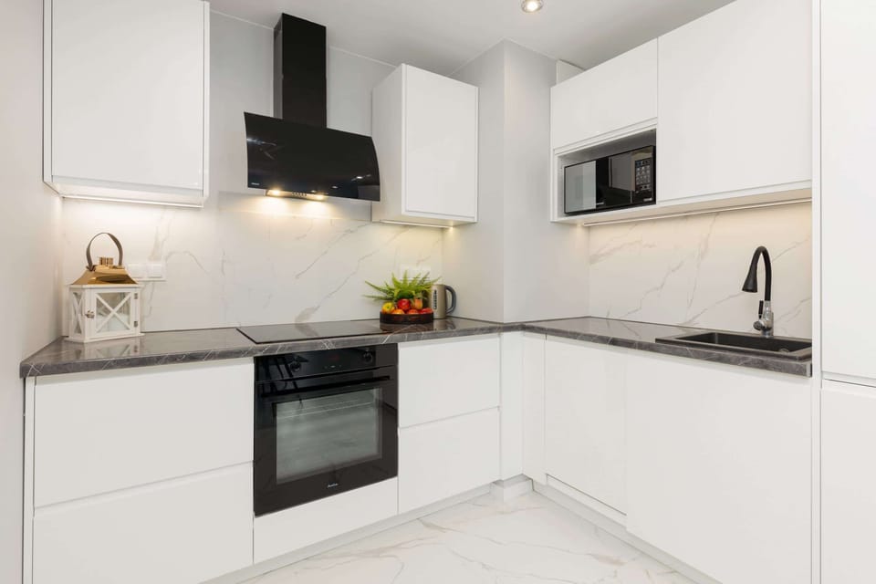 A modern kitchen with sleek white cabinets, marble countertops, and black accents.
