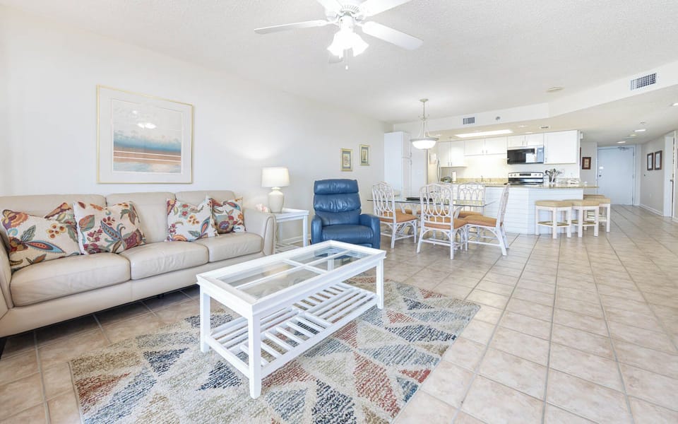 Living area features a light-colored sofa with decorative pillows, a glass coffee table, and a dining area with seating
