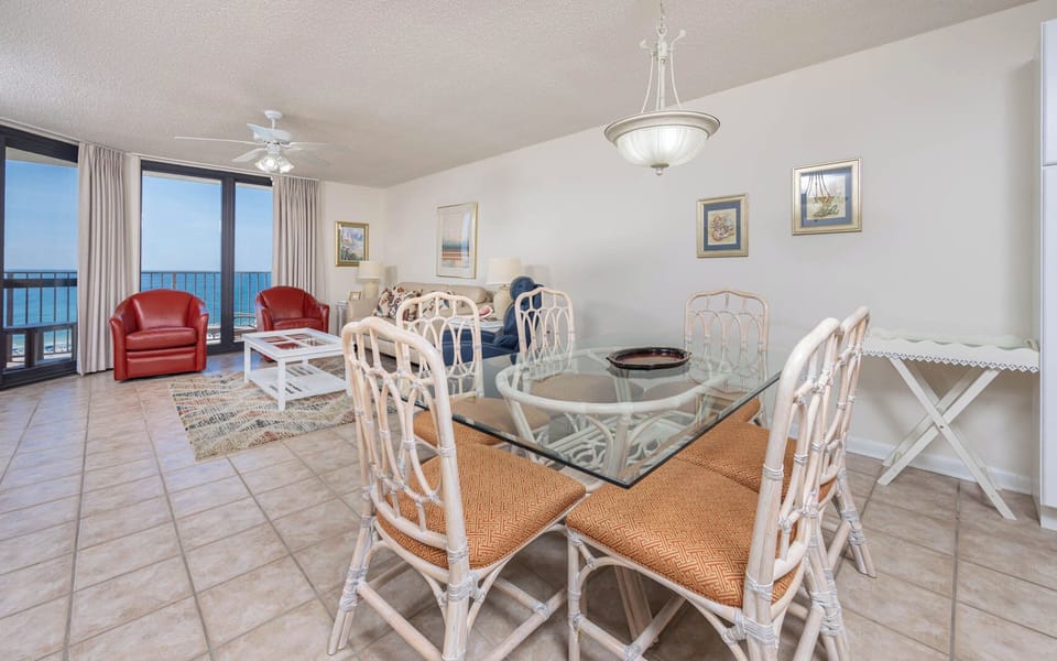 Dining area features a glass-top table with wicker chairs, complemented by red leather armchairs and a scenic gulf view