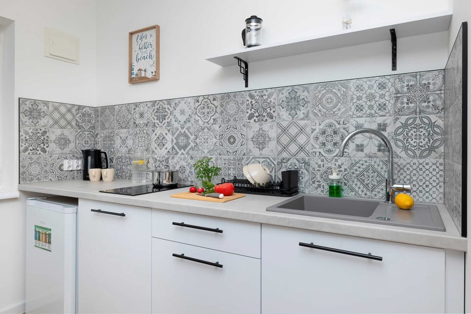 A small yet functional kitchen with white cabinets and a neutral backsplash. The countertop is accessorized for meal prep.