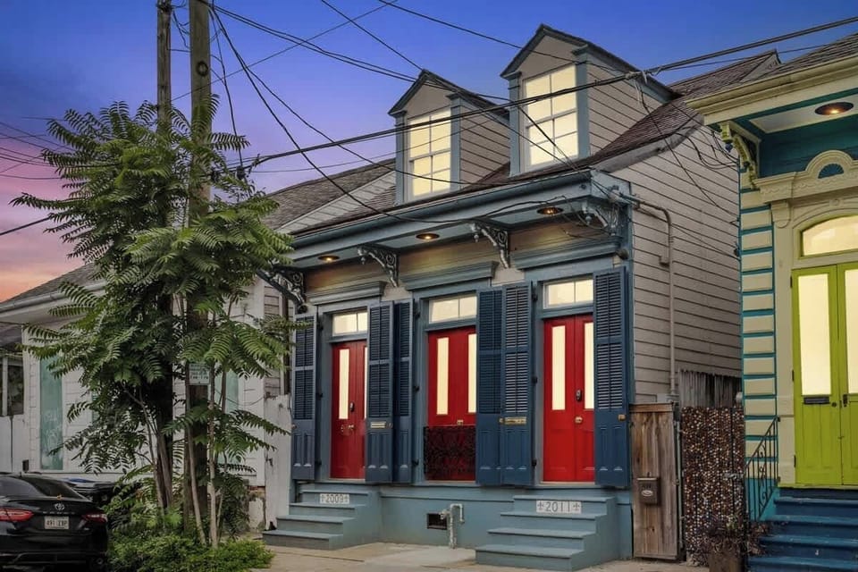 A classic Creole façade glows at dusk with bold red doors, shuttered windows, and historic trim. Just steps from Frenchmen Street and an easy walk to the French Quarter’s music, food, and nightlife.