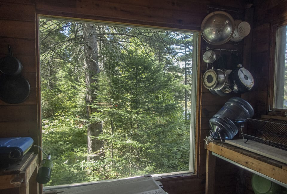 window overlooking west with kitchen sink, pots/pans and a water jug supply