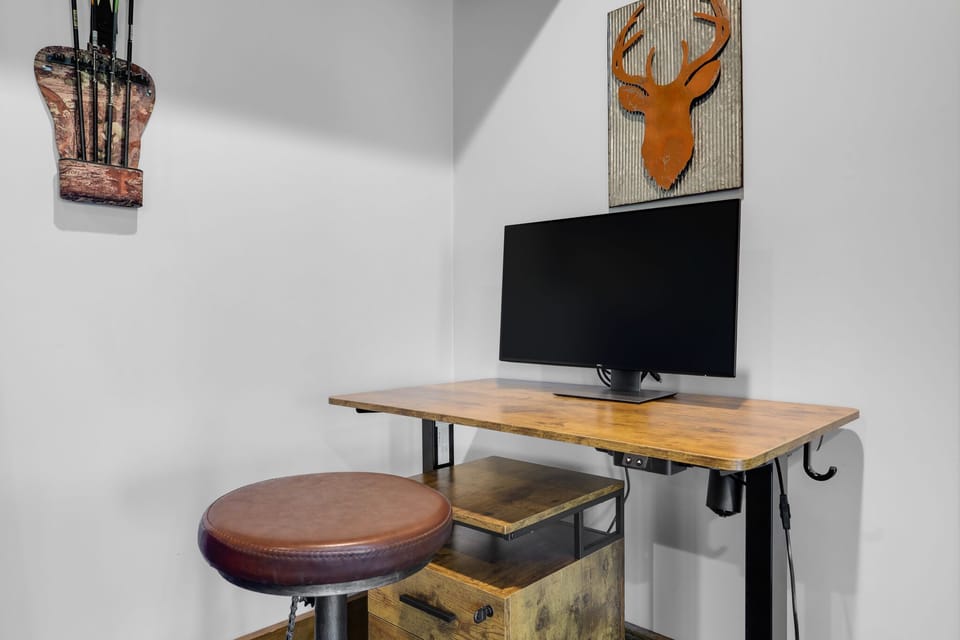 Sitting/standing desk with large monitor located in game room.
