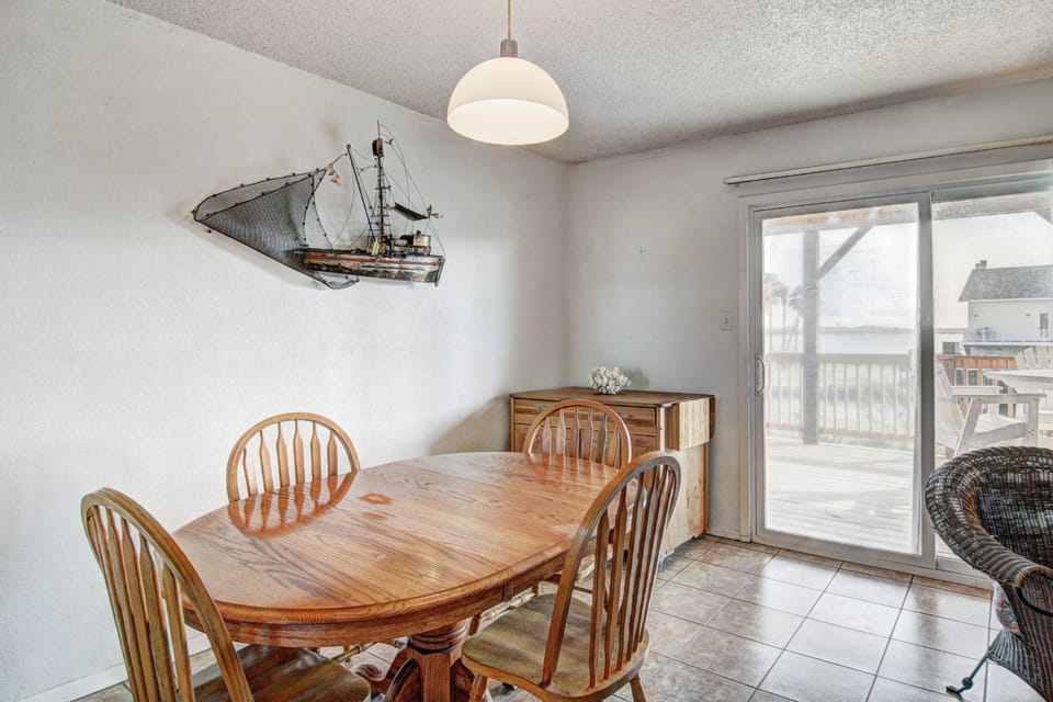 Gather around your charming dining table featuring coastal nautical decor and bright natural light streaming through sliding glass doors.