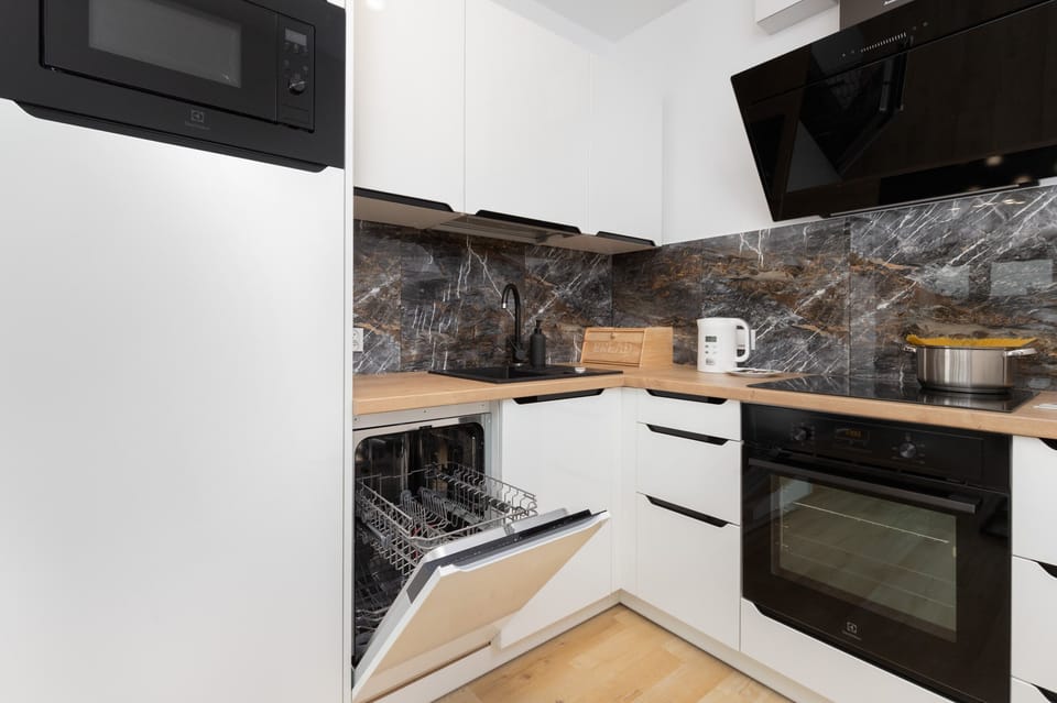 Sleek kitchen with white cabinets, a built-in oven, and a marble-patterned backsplash, fully equipped for meal preparation.

