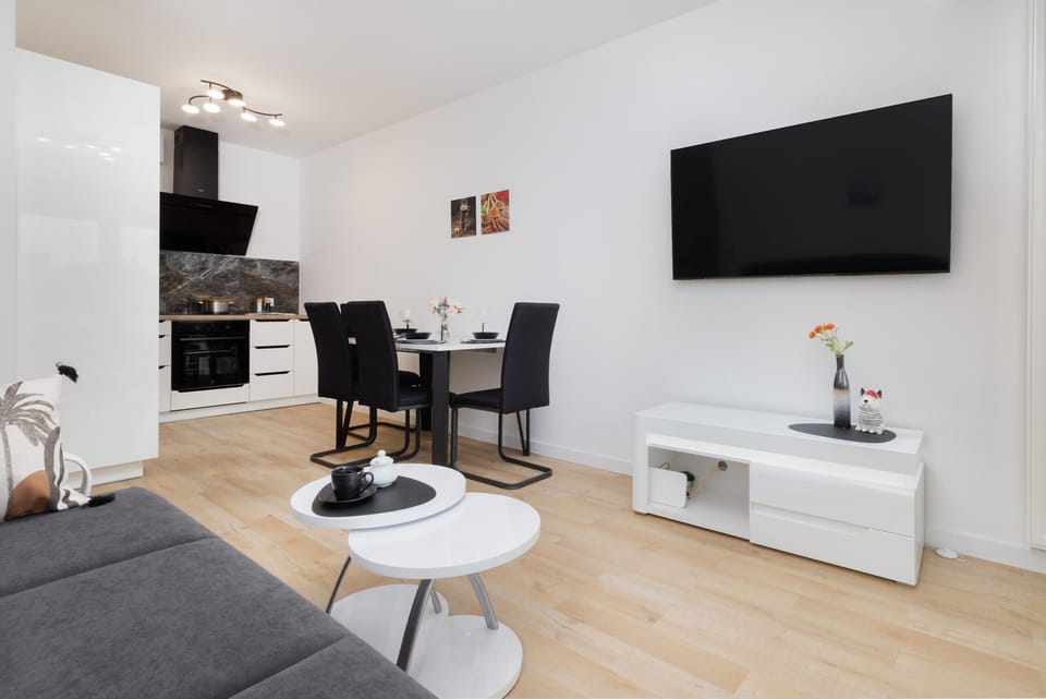 Bright open-plan living area featuring a dining table, flat-screen TV, and modern furnishings for a functional and stylish space.
